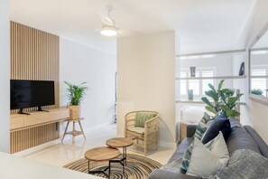 A modern living room with a flat-screen TV, wooden paneling, a wicker chair, a grey sofa, and a ceiling fan. - Chic Sea Point Retreat Walk to the Promenade Caf s (Cape Town)