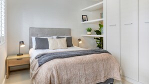 Une chambre bien rangée, avec un lit, des tables de chevet, une armoire et des étagères ornées de plantes.