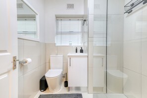 A modern bathroom with a glass shower enclosure, a toilet, a sink, and a window with blinds. - Chic Sea Point Retreat Walk to the Promenade Caf s (Cape Town)