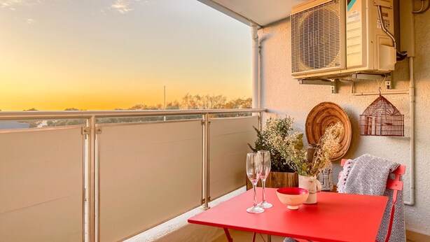 A balcony with a red table, two wine glasses, a bowl, and a red chair. - Modern One Bed Central Green Point Stadium (Cape Town)