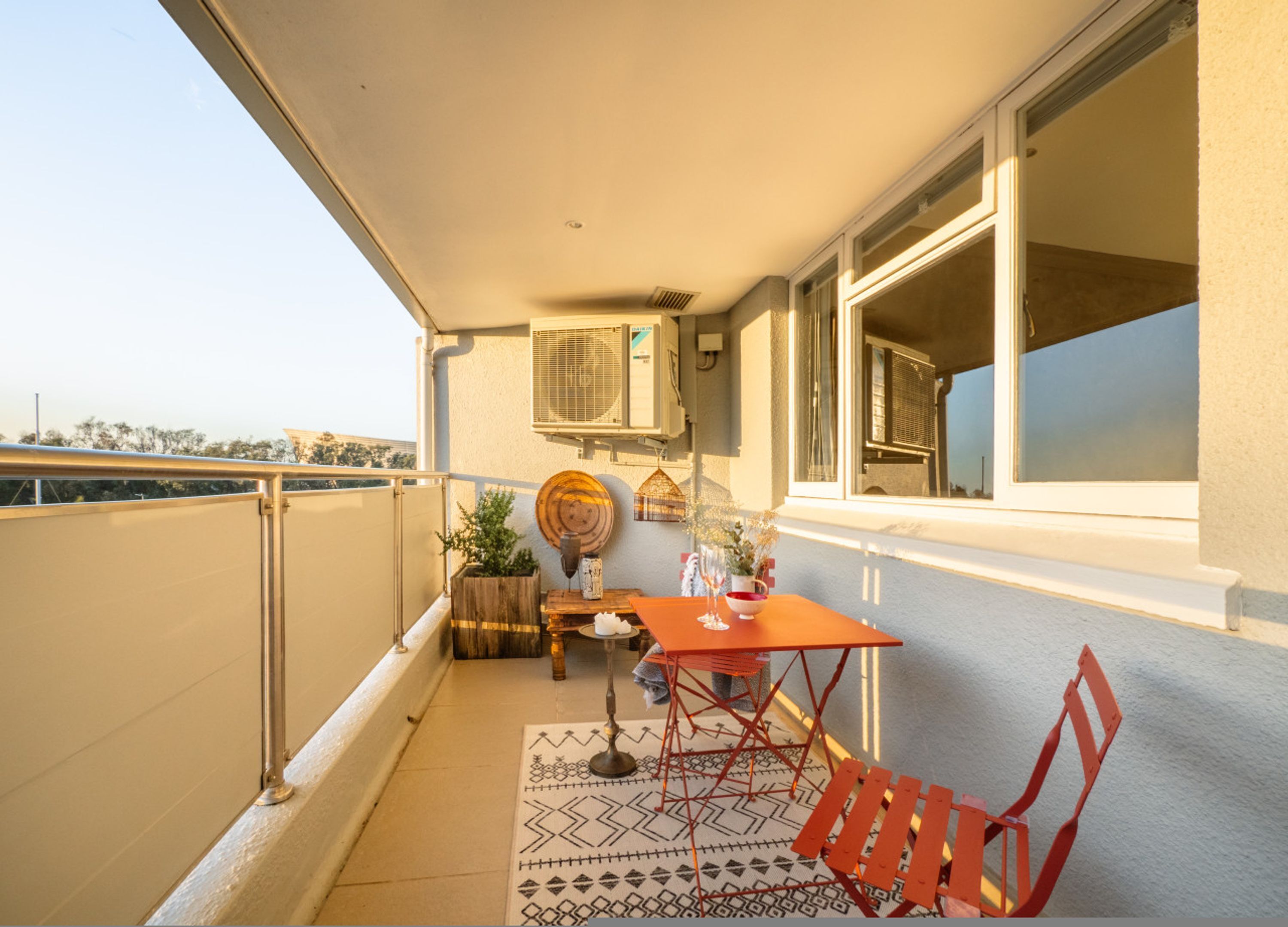 A balcony with a table, chairs, a potted plant, and a decorative wall piece.