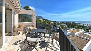 A balcony with a table and chairs, overlooking a coastal view. - Elegant Camps Bay Eco Pool Sauna Views (Cape Town)