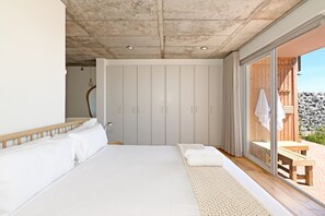 Ein Schlafzimmer mit einem großen Bett, einer hölzernen Sitzbank und einer Schiebeglastür, die zu einem Außenbereich führt.