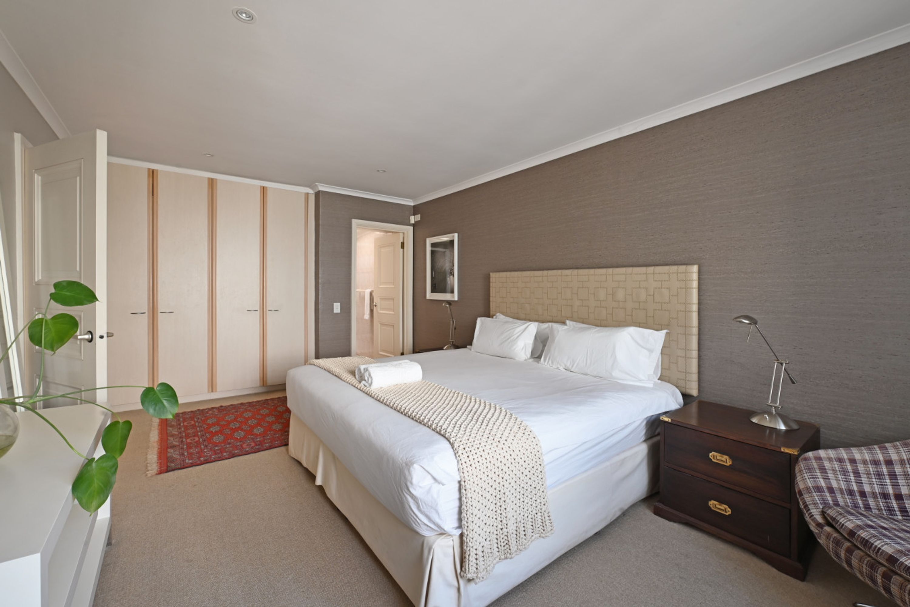 A bedroom with a large bed, a nightstand, a dresser, and a door leading to a closet.