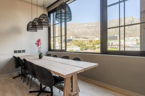 A conference room with a large table, black chairs, and hanging pendant lights. - East City Modern Apt Co-working (Cape Town)