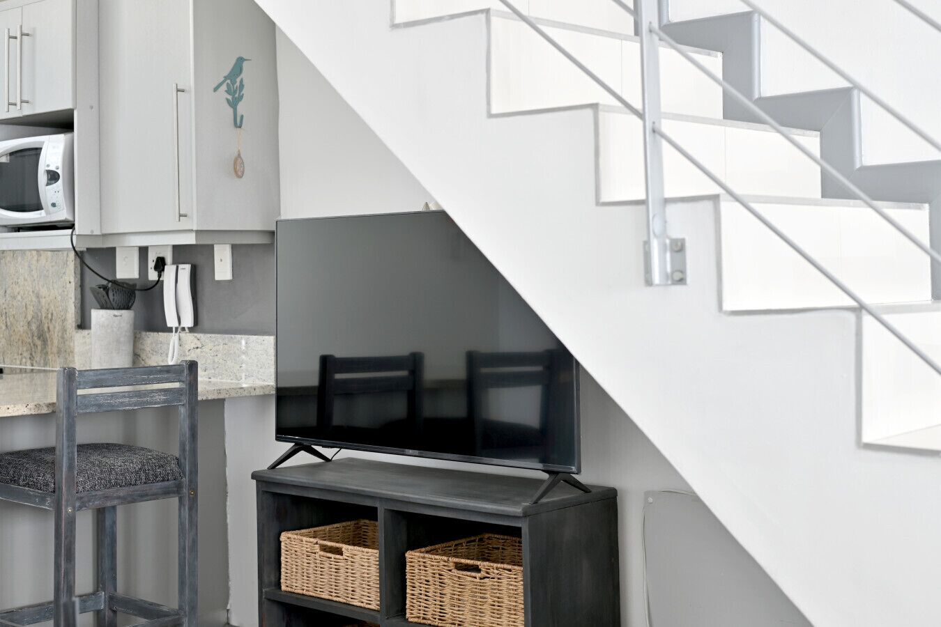 A modern kitchen with a built-in microwave, a flat-screen TV, and wicker baskets on a dark wooden shelf.