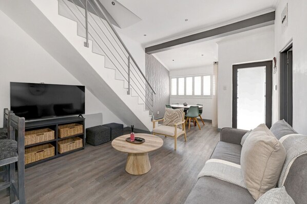 Un salon moderne avec un escalier, un téléviseur à écran plat, une table basse ronde en bois et un canapé.