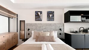 Una camera da letto moderna con un letto grande, una cassettiera in legno, una scrivania integrata e un angolo cottura.