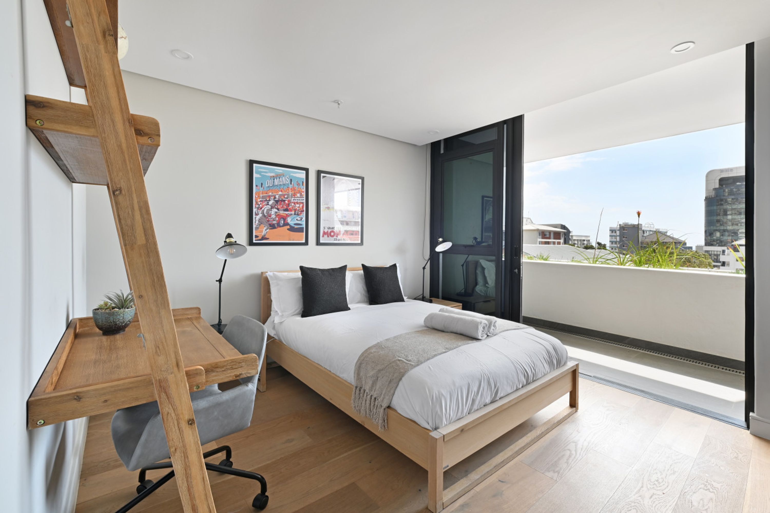 A modern bedroom with a wooden bed, a desk, and a city view.