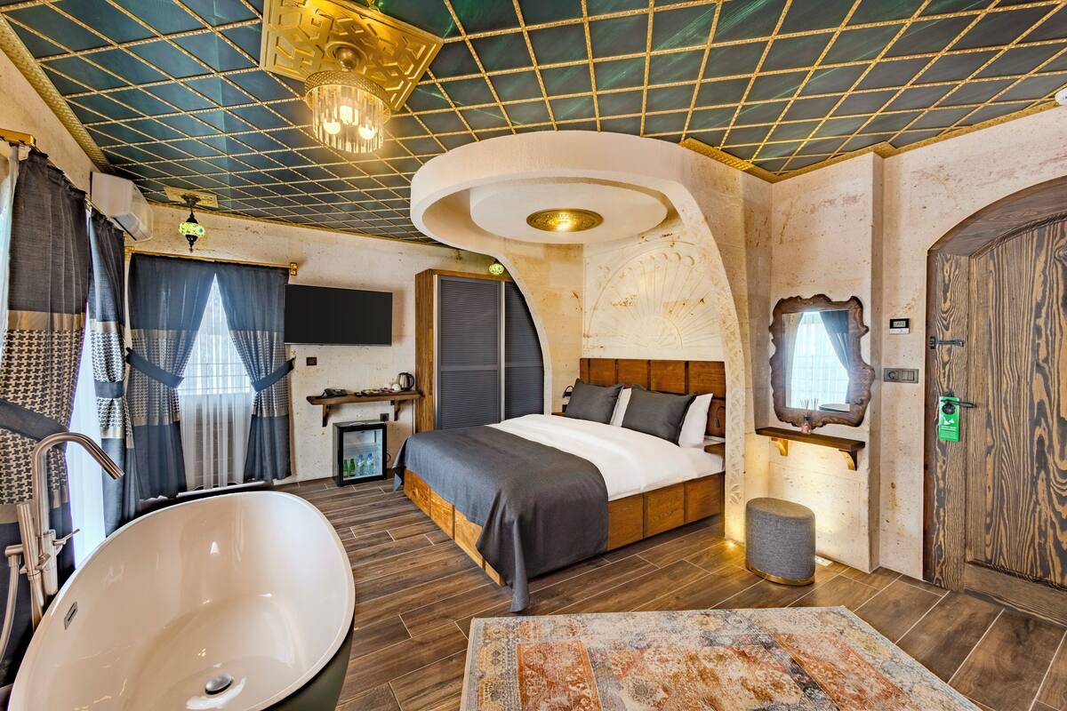 A modern bedroom with a large bed, a bathtub, and a unique ceiling design.