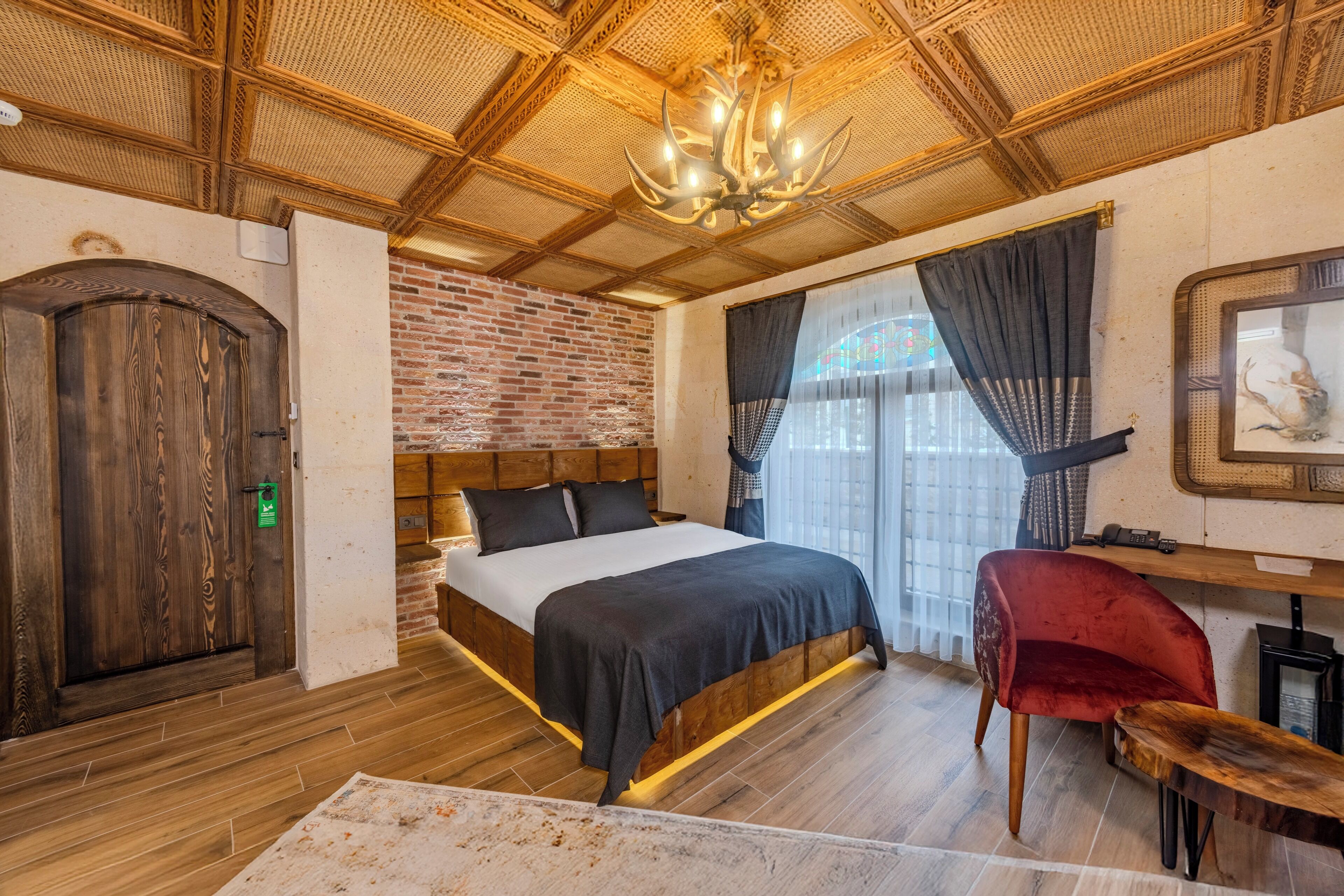 Un dormitorio con cama de madera, pared de ladrillo, lámpara de araña y una silla roja.