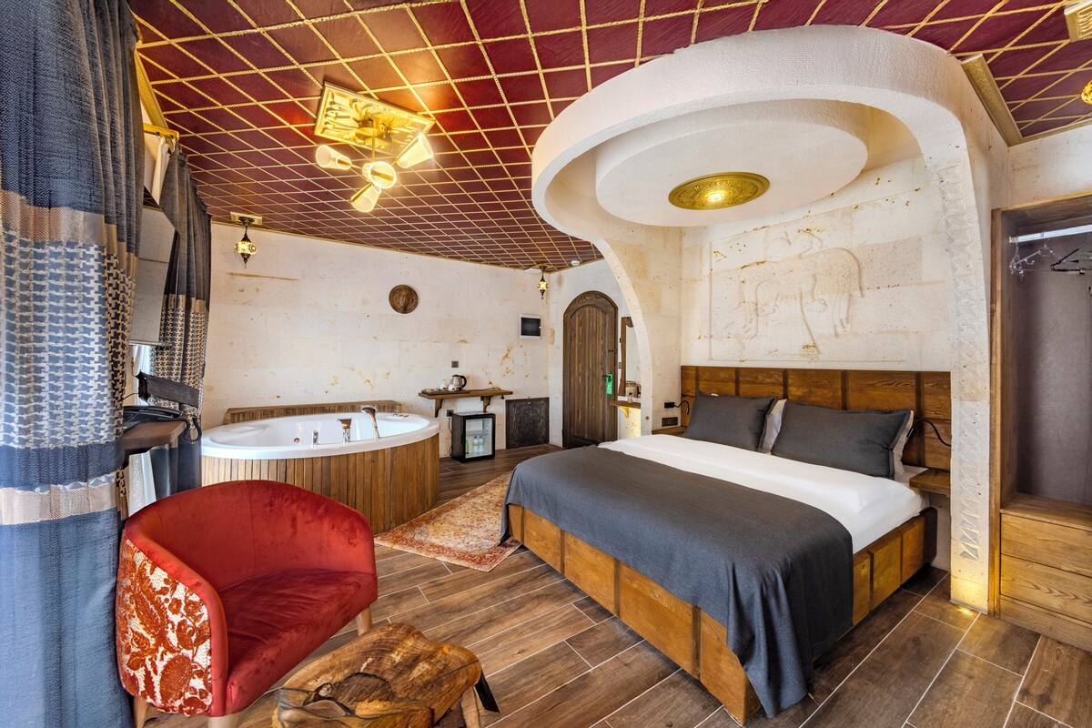 A bedroom with a large bed, a red chair, a wooden floor, a bathtub, and a sink.