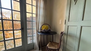 Ein Zimmer mit einer Tür, die zu einem Garten führt, ein kleiner runder Tisch mit einem Stuhl und eine Vase mit gelben Blumen.