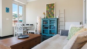 Een kamer met een bed, een bureau, een stoel, een kast en een raam met uitzicht op gebouwen.