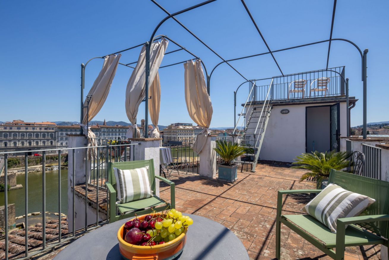 A rooftop terrace with a table, chairs, and a bowl of fruit.