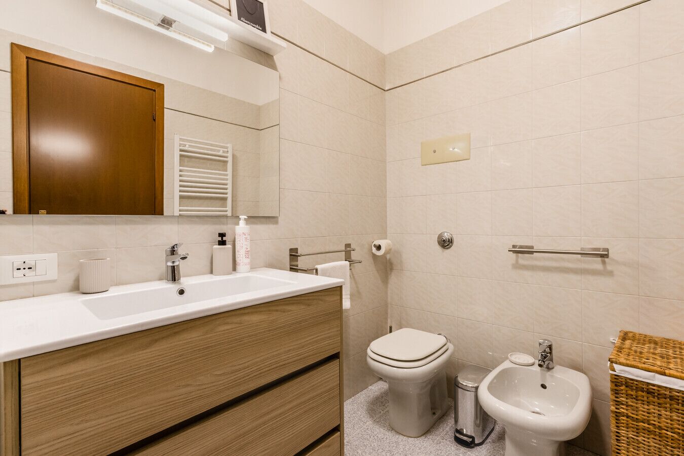 A modern bathroom with a wooden vanity, a sink, a toilet, and a bidet.
