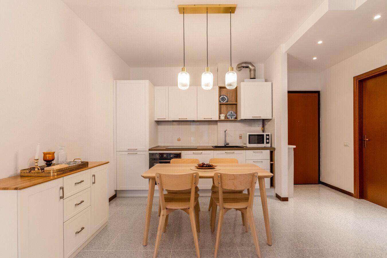 Una cocina compacta con armarios blancos, una mesa de comedor de madera y un microondas.