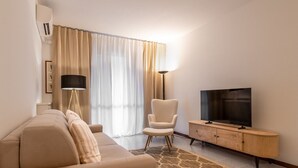 Ein modernes Wohnzimmer mit Sofa, Sessel, Fernseher und Lampe.