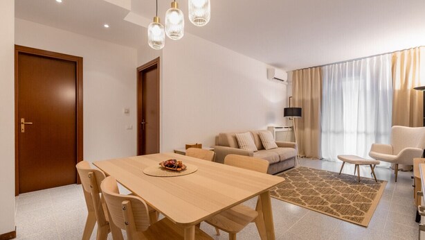 Ein modernes Wohnzimmer mit einem Holzesstisch, einem beigen Sofa und einem gemusterten Teppich.