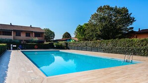 Ein rechteckiger Pool mit Holzterrasse, umgeben von Hecke und Zaun.