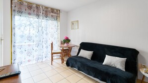 Ein Zimmer mit einem dunkelgrauen Sofa, einem kleinen runden Tisch mit einer rosa Blume und einem Sessel.