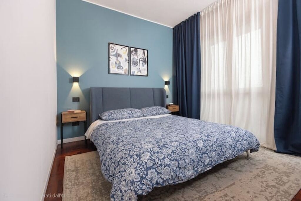 Een slaapkamer met een bed, twee wandlampen, een nachtkastje en een raam met gordijnen.