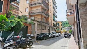 Une rue résidentielle bordée de voitures et de motos garées, des immeubles à plusieurs étages dotés de balcons et un ciel dégagé.