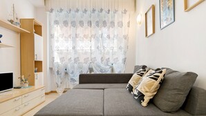 Un salon moderne avec un canapé gris, des étagères en bois, un téléviseur à écran plat et des rideaux à motifs.