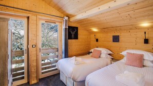 Quarto de cabana de madeira com duas camas, uma janela grande e uma porta que dá para o exterior.