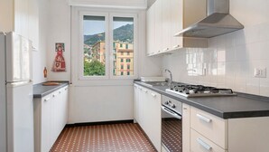 Une cuisine compacte avec des meubles blancs, une cuisinière à gaz, une fenêtre donnant sur des immeubles et un sol à motifs.