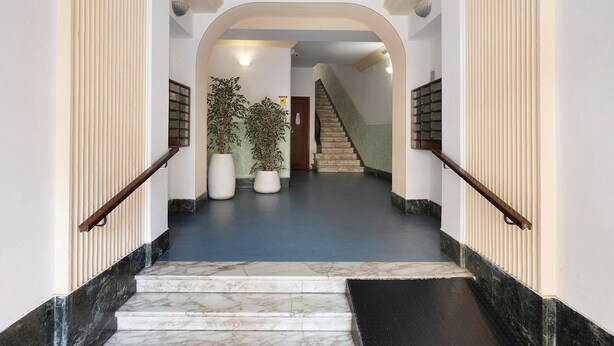 Un escalier en marbre mène à un palier agrémenté de plantes en pot, et on aperçoit un autre escalier au fond.