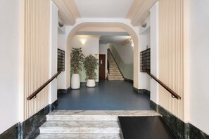 Una scalinata in marmo conduce a un pianerottolo con piante in vaso e una vista su un'altra scala sullo sfondo.