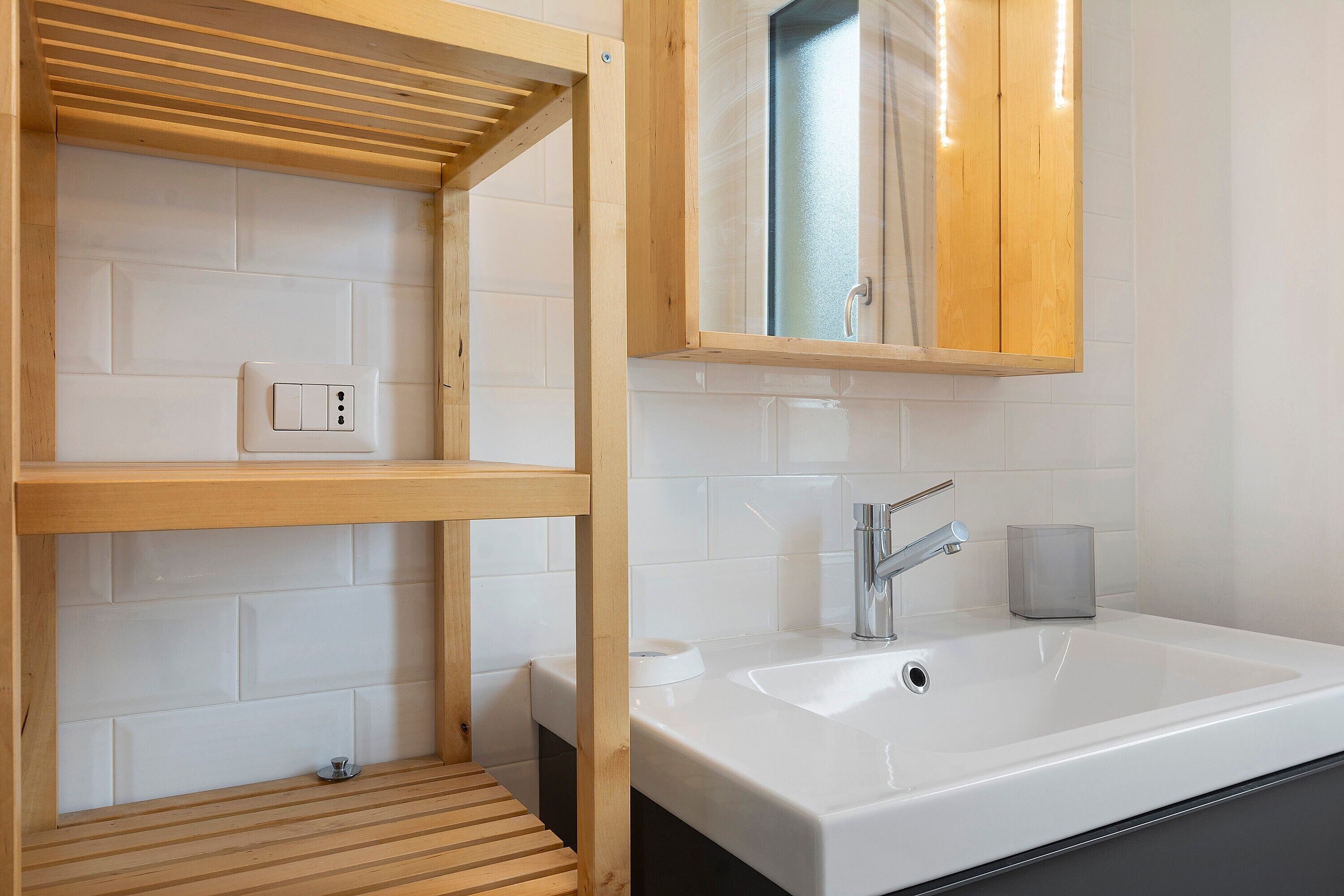 A bathroom with a wooden shelf, a sink, a mirror, and a towel rack.
