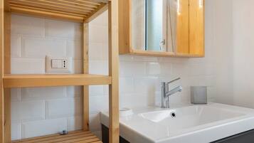 A bathroom with a wooden shelf, a sink, a mirror, and a towel rack.