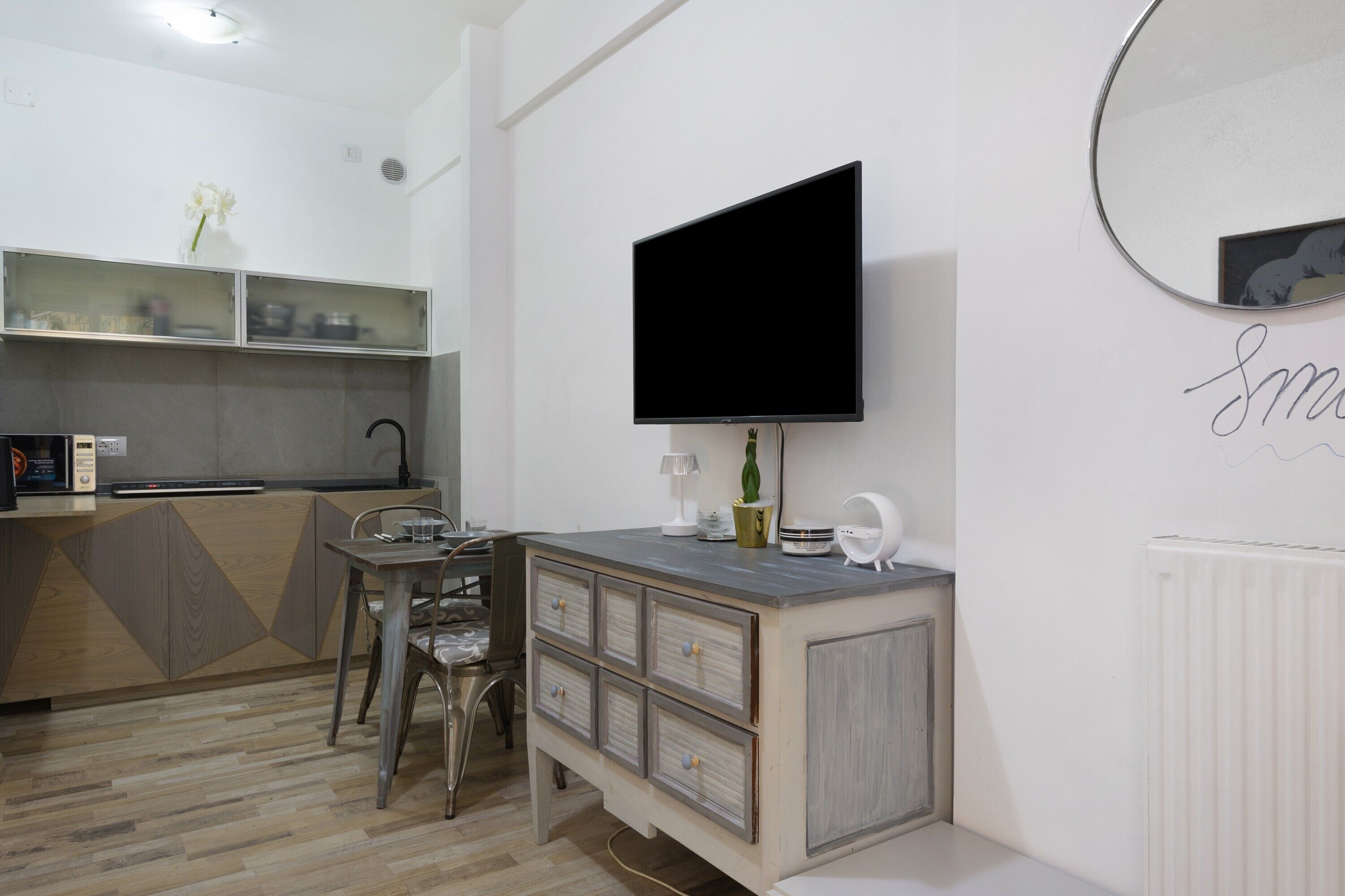 Una cucina moderna con piano cottura integrato, zona pranzo con tavolo e sedie, e un grande televisore a schermo piatto montato a parete.