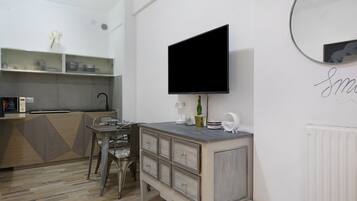 Una cucina moderna con piano cottura integrato, zona pranzo con tavolo e sedie, e un grande televisore a schermo piatto montato a parete.