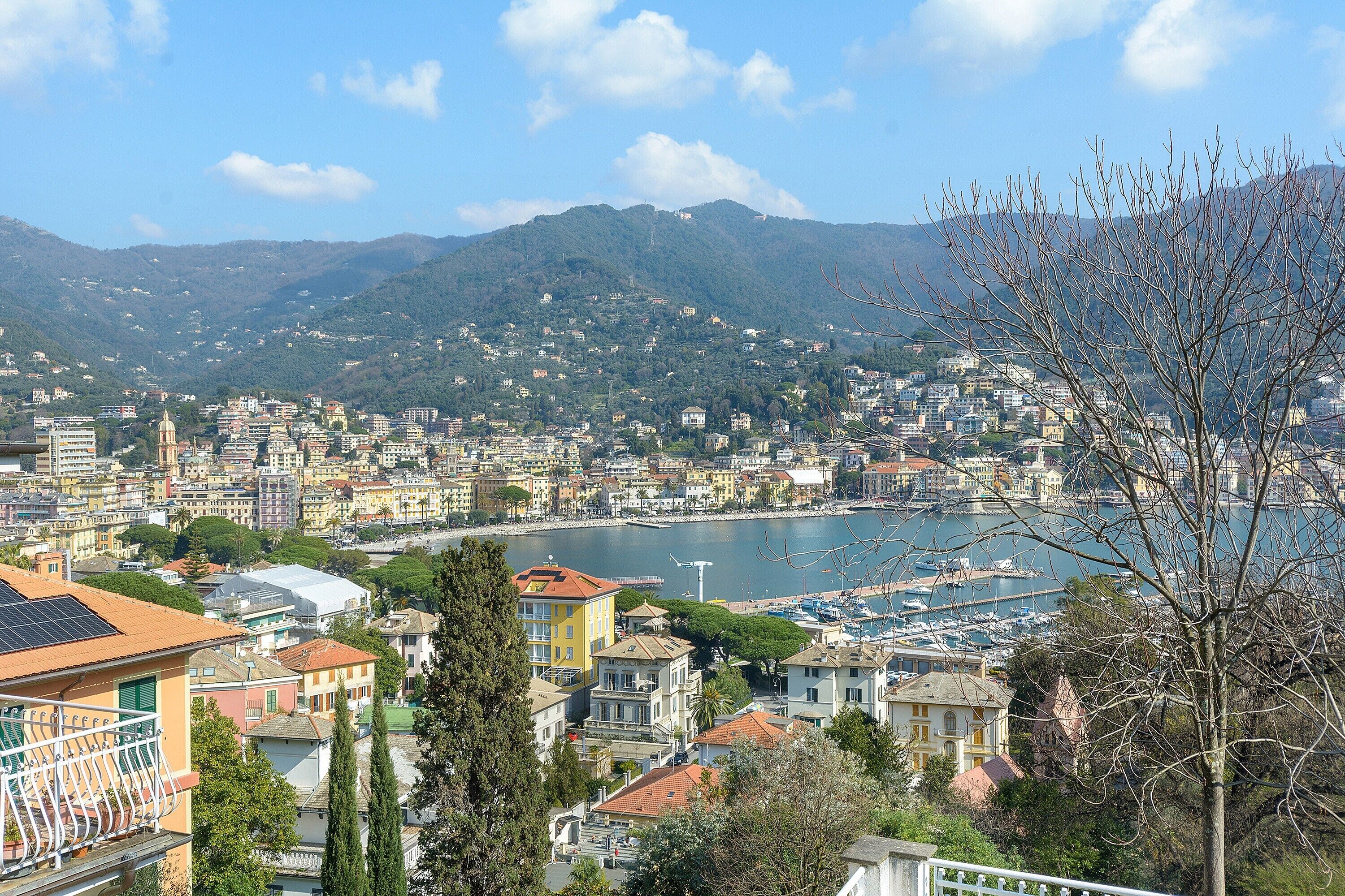 A coastal cityscape with buildings, a marina, and mountains in the background.