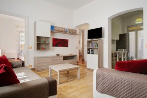 Un salon moderne comprenant un canapé, une table basse, un téléviseur et un coin cuisine visible à travers une arche.