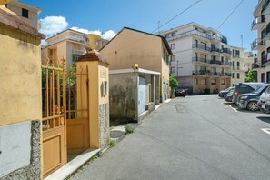 Une rue étroite bordée de voitures garées, une entrée fermée par un portail et des immeubles d’habitation dotés de balcons.
