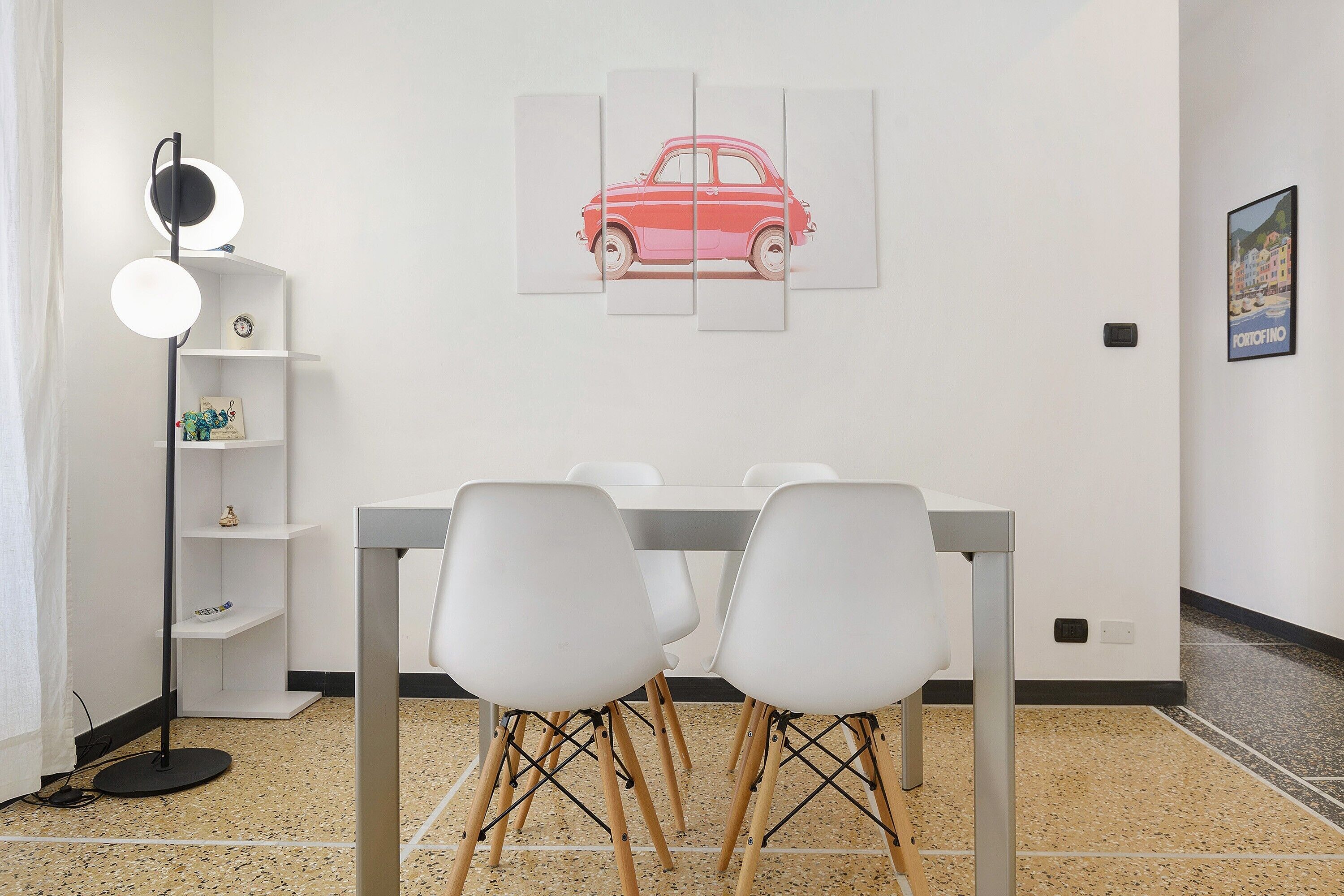 Een eetgedeelte met een tafel, stoelen en een schilderij van een auto aan de muur.