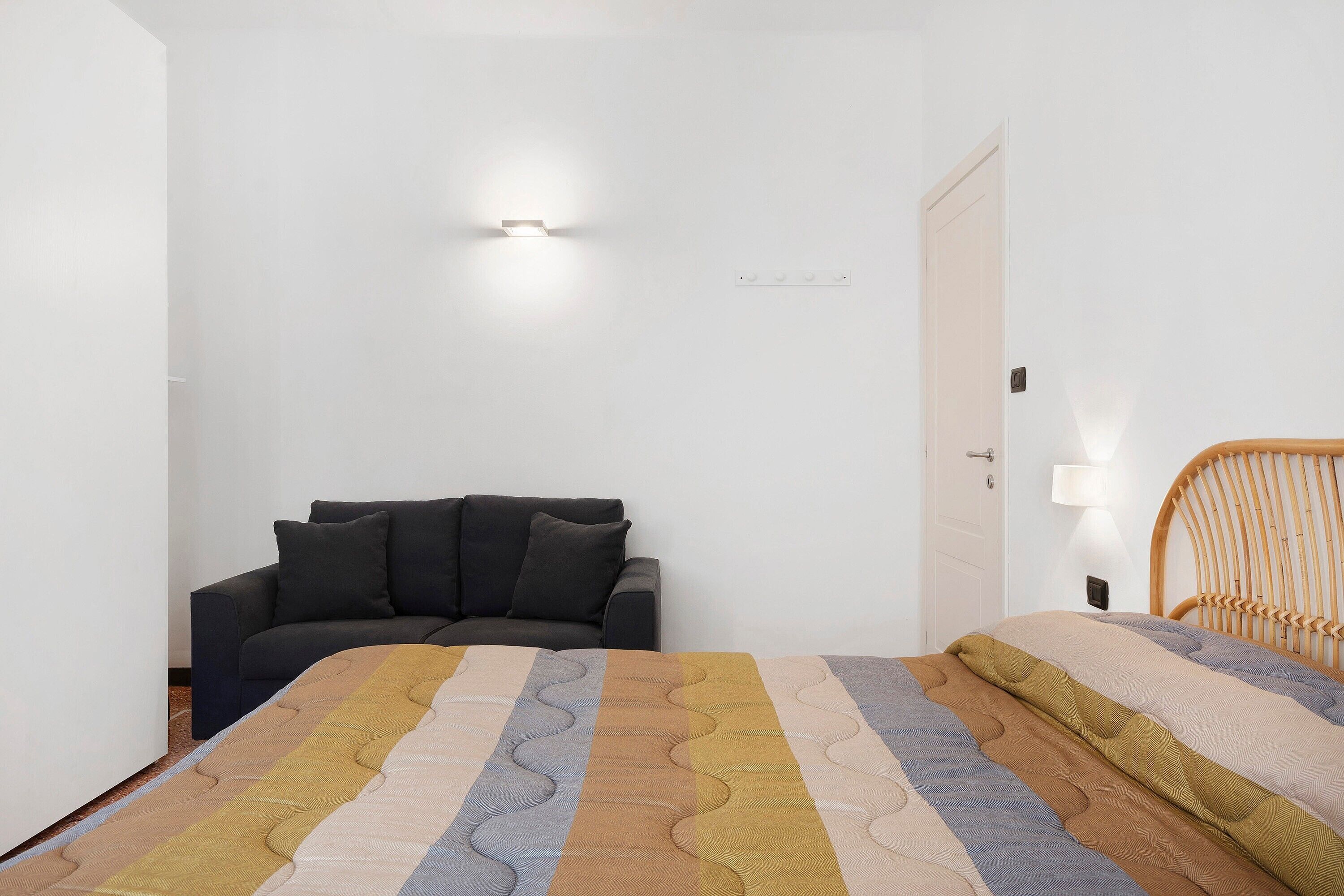 Een slaapkamer met een bed, een slaapbank, een nachtkastje en een wandlamp.