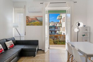 Un salon moderne avec un canapé, une table à manger et une vue sur un balcon donnant sur des immeubles.
