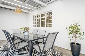 A dining area with a glass table, metal chairs, a potted plant, and a window with white frames. - Winelands Getaway (Stellenbosch)