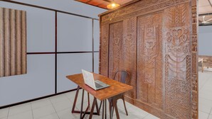 A room with a wooden table, a laptop, and a decorative wall panel. - Hotel O near Trans Studio Theme Park formerly Sunset Cozy (Kuta)