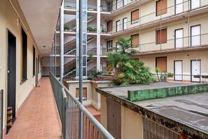 Un edificio residencial de varios pisos con balcones, plantas en macetas y un corredor con baldosas.