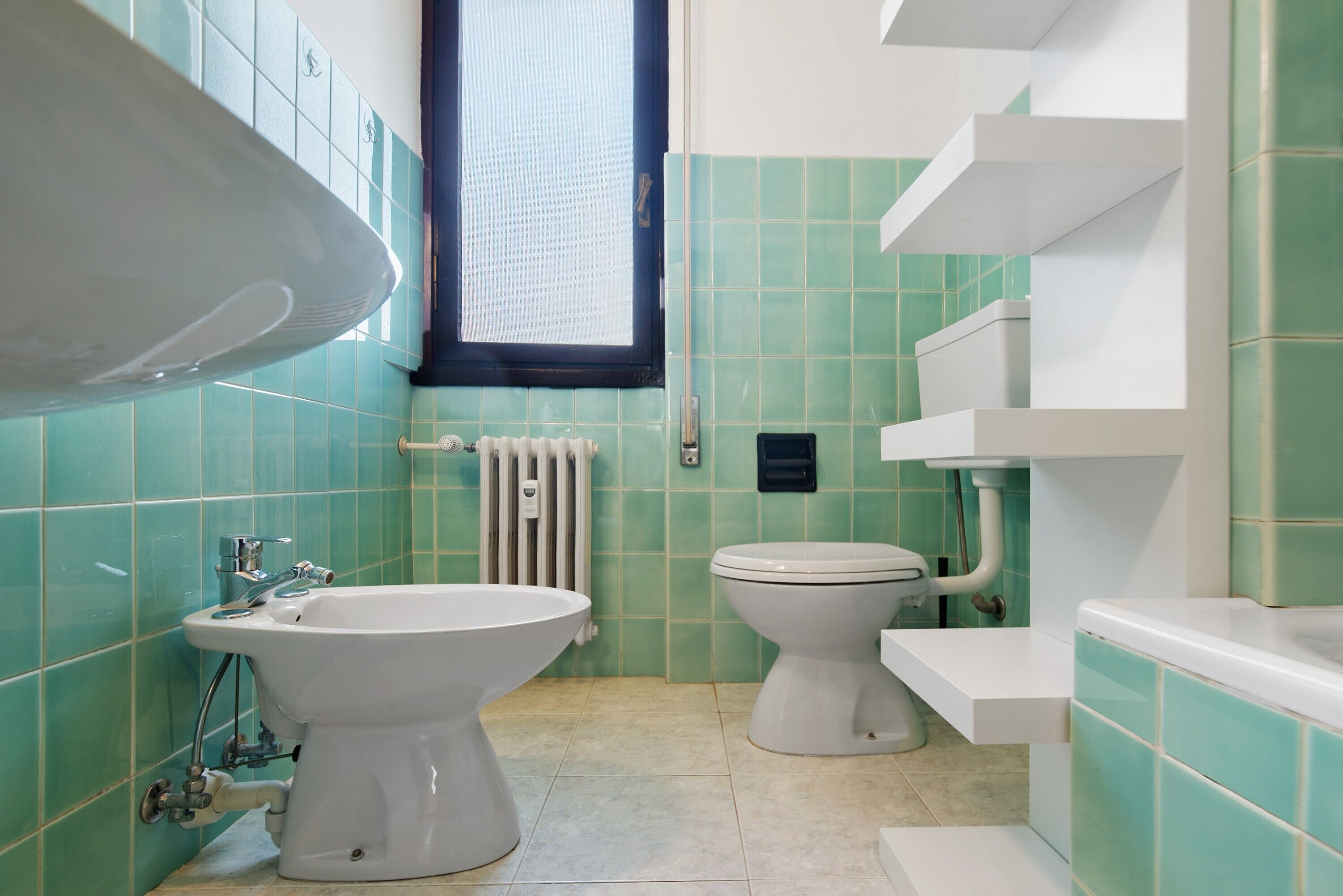 Ein Badezimmer mit einer Bidet-Einrichtung, Toilette und einem Fenster.
