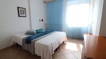 A bedroom with a bed, a dresser, a framed picture on the wall, and a window with blue curtains.