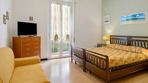 Un dormitorio con una cama, un televisor sobre un aparador de madera, un sofá y una ventana con cortinas.