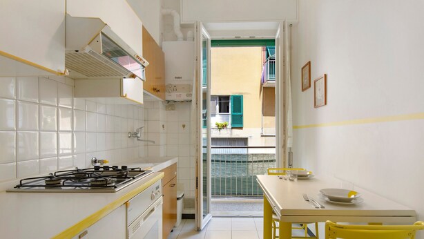 Cocina compacta con estufa a gas, un lavamanos y zona de comedor con mesa y sillas amarillas.