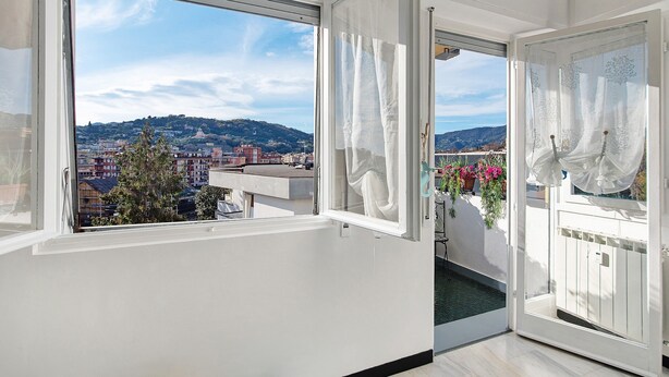 Ein Balkon mit Blick auf eine Stadtansicht, eine Tür und ein Fenster mit Vorhängen.